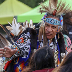 A dancer in traditional regalia, featuring intricate beadwork and feathers, prepares to perform.