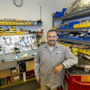 Miguel “Mickey” Galindo, Maintenance/Facilities Tech II at CSUN's Student Recreation Center, stands in the SRC's machine shop, surrounded by tools and a workbench.