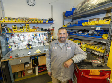 Miguel “Mickey” Galindo, Maintenance/Facilities Tech II at CSUN's Student Recreation Center, stands in the SRC's machine shop, surrounded by tools and a workbench.