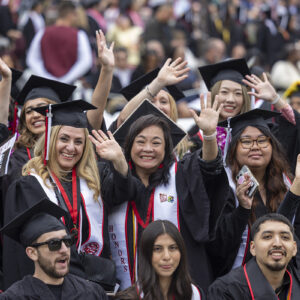 Students in caps and gowns smile and wave at the camera at Commencement, 2024.
