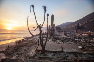 A burned structure with the ocean in the background.
