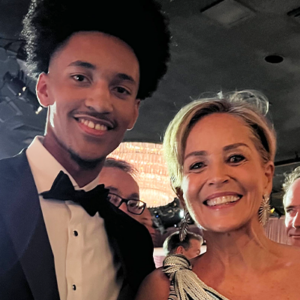 Rutledge, dressed in a black tuxedo, poses alongside actress Sharon Stone, just an hour before showtime, in warm lighting.