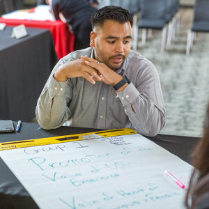 Freddie Sanchez sitting at a table and talking, with a large notepad in front of him.