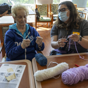 Two people sit side by side with crochet hooks and yarn.
