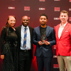 Director of Athletics Shawn Chin-Farrell stands on stage with the late Joseph Vaughn’s mother, son, and best friend/teammate. In front of a CSUN Athletics backdrop, Vaughn’s son proudly holds the award in his honor.