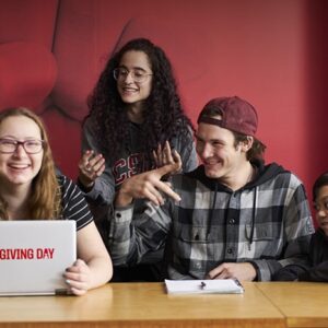 Students gathered around computer with "Giving Day" graphic.