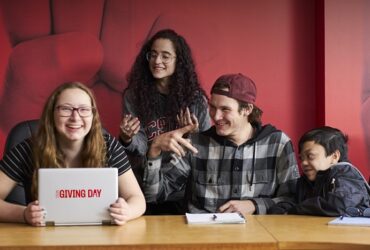 Students gathered around computer with "Giving Day" graphic.