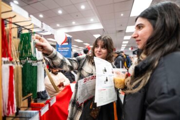 Two students looking at various graduating tassels and one the students holding a tassel to get a closer look at it.