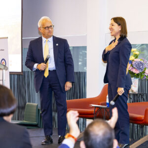 Fred Gaines, former mayor of Calabasas, stands next to California Lt. Gov. Eleni Kounalakis on stage, as people applaud in the foreground. Both Gaines and Kounalakis are holding microphones.