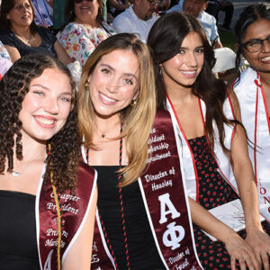 Three students wearing graduation sashes smile for the camera.