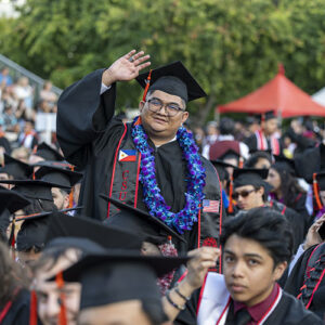 A student in cap and gown waves hello from the crowd.