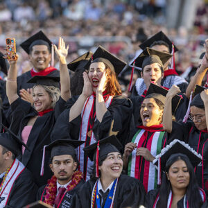Graduates wearing caps and gowns cheer in the audience during the commencement ceremony.