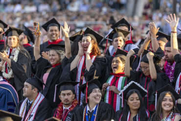 Graduates wearing caps and gowns cheer in the audience during the commencement ceremony.