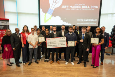Group gathered on stage with Tim Attewell in center, with oversized check.