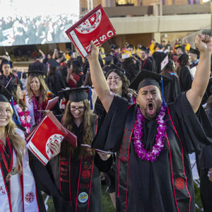 College graduates wave and cheer at their commencement ceremony.