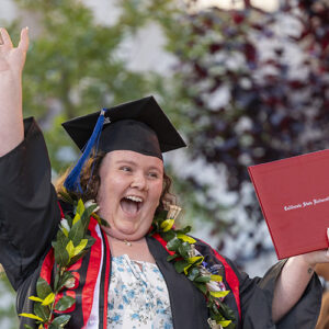 A CSUN graduate waves and cheers with diploma in hand.