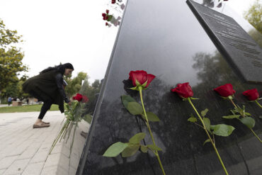 Red roses lean against the base of the Matador Statue with a staff member in the background.