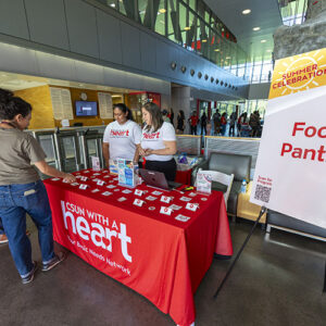 Two women stand behind a table draped in red with "CSUN with a heart."