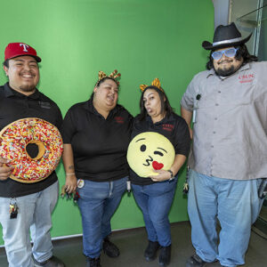 Four staff members stand together, one posing with a donut pillow and another holding an emoji pillow.