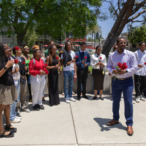 Ryan Mason stands in front of a group of students, all holding roses.