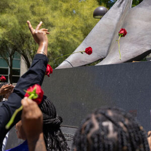 Hands toss roses toward the base of the Matador statue.