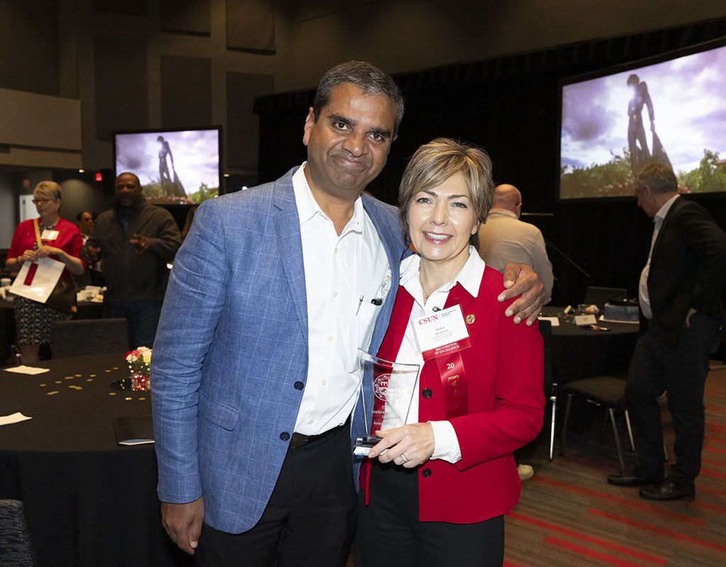 Ranjit A. Philip and Helen Heinrich pose, smiling for a photo. Helen Heinrich holds a glass plaque.