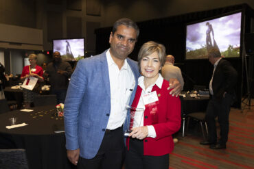 Ranjit A. Philip and Helen Heinrich pose, smiling for a photo. Helen Heinrich holds a glass plaque.