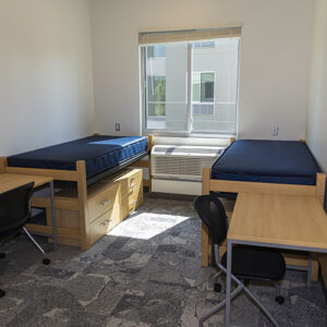 Interior of student bedroom, with single beds on each side of the room and desks in the foreground.