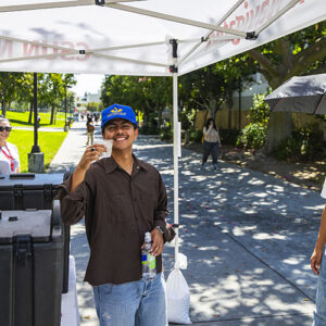 A student smiles and holds his water cup up to the camera at a CSUN Navigator pop-up tent.
