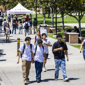 Three smiling students walk together on walkway between the University Library and the University Student Union.