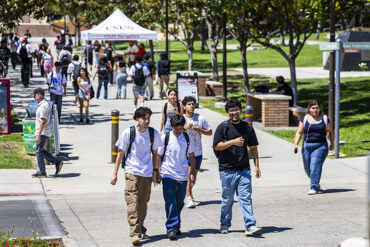 Three smiling students walk together on walkway between the University Library and the University Student Union.