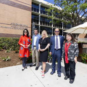 Five people pose in front of CSUN's Jacaranda Hall and the new Andrew J. Anagnost College of Engineering and Computer Science name.