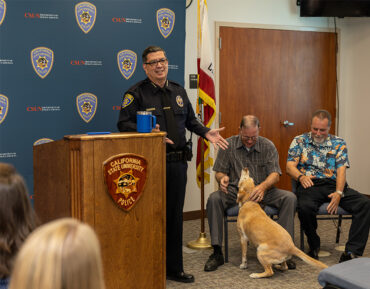 Department of Police Services Chief Alfredo B. Fernandez stands to the side of the podium, with Sergeants Abney and Messmore and K9 officer Daisy off to the right.