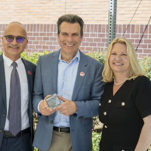 Andrew Anagnost holds a glass cube that commemorates the naming of the Andrew J. Anagnost College of Engineering and Computer Science. He is standing flanked by Houssam Toutanji and CSUN President Erika D. Beck.
