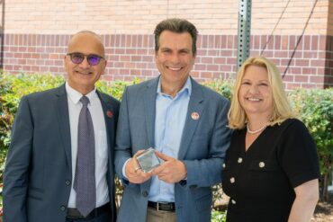 Andrew Anagnost holds a glass cube that commemorates the naming of the Andrew J. Anagnost College of Engineering and Computer Science. He is standing flanked by Houssam Toutanji and CSUN President Erika D. Beck.