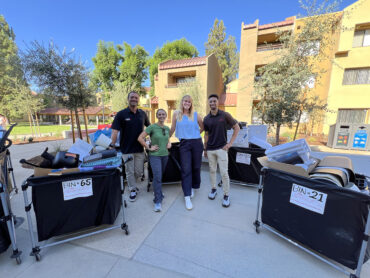 Group of four people pose for a photo among large bins filled with household items.