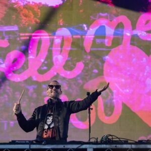 Galantis stands on stage, smiling with his arms raised, with video display in background.