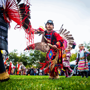Boy in traditional regalia dancing on grass with others