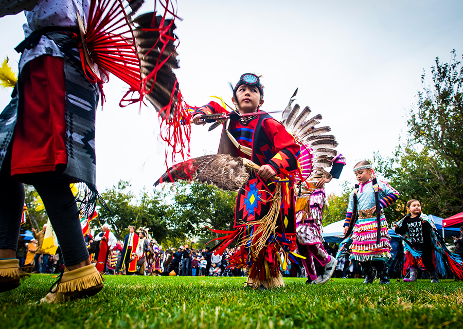 Boy in traditional regalia dancing on grass with others