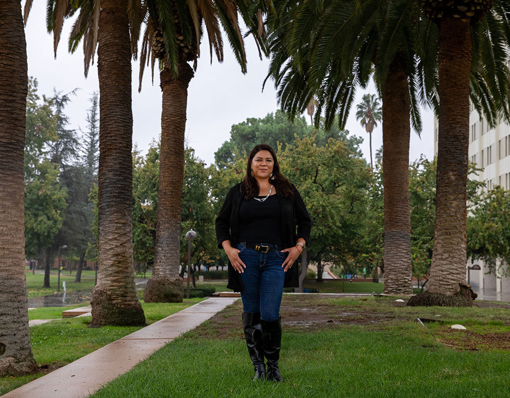 Jenee Ornelas '19 stands between rows of palm trees outside the University Library.