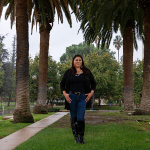Jenee Ornelas' stands in the rain between rows of palm trees in front of the University Library.