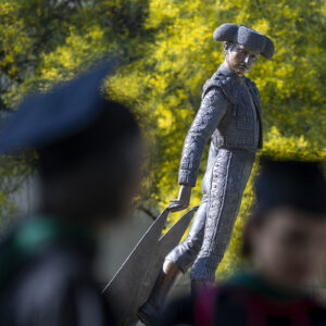 Matador statue in the background with students wearing caps and gowns in the foreground.