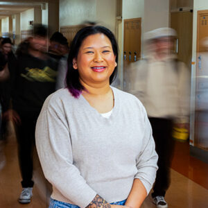 Arby Jean Wolkov smiles and poses for the camera, with people in hallway in background.