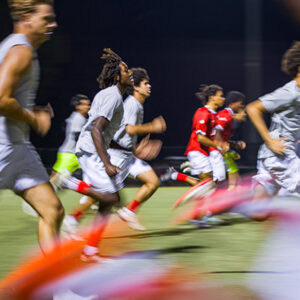 Men's soccer team members run drills together in a line across the field.