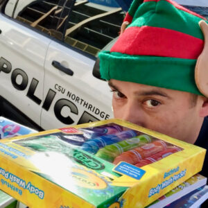 Person holding a stack of toys with police car in the background.