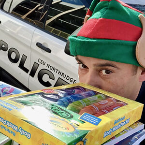 Person holding a stack of toys with police car in the background.