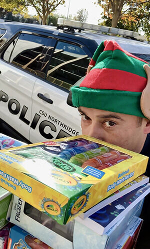 Person holding a stack of toys with police car in the background.