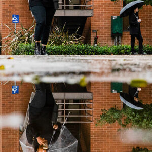 Students in background, with umbrellas, are reflected in large puddles in foreground.