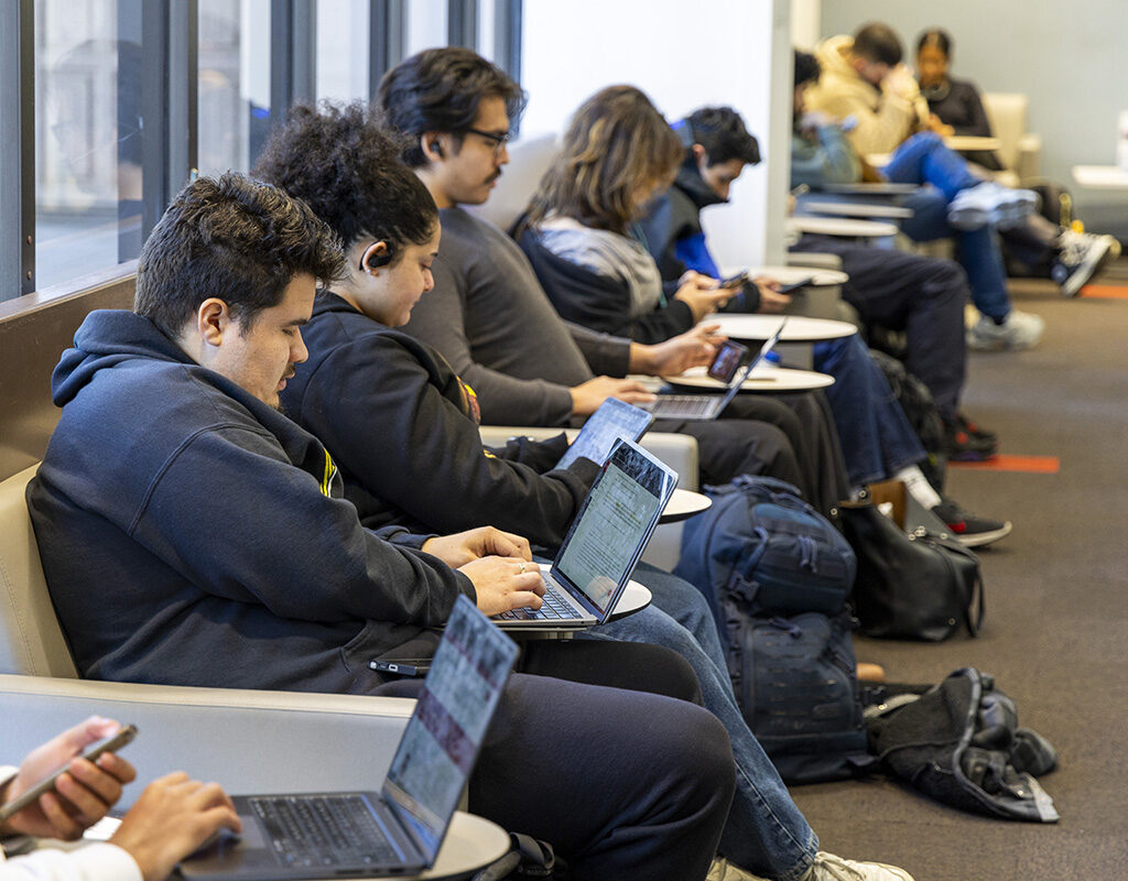 Students sit, using laptops.
