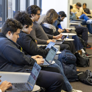 Students sit, using laptops.